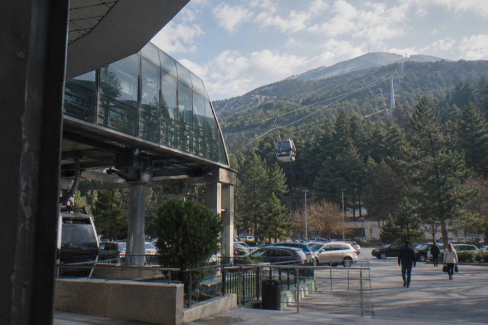 A cable car cabin rising above pine trees toward the ridge of Mount Dajti