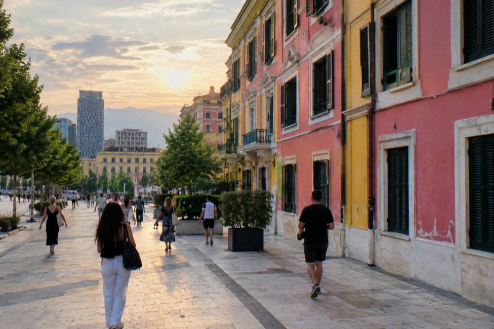 People walking along a colourfully painted building facade on a Tirana street in the evening