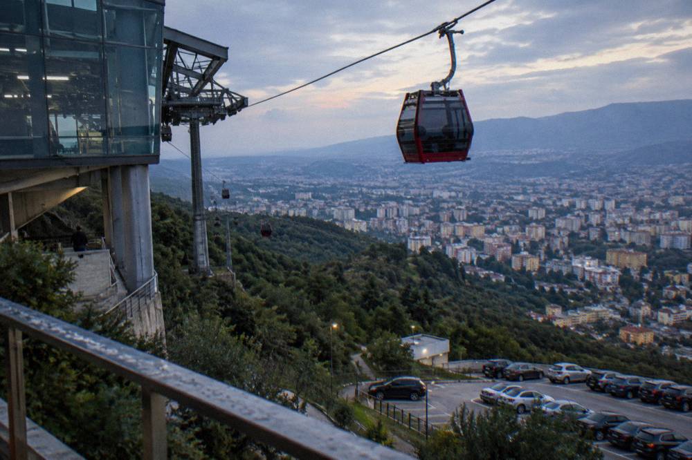 A red cable car cabin suspended above a forested mountain slope above a city basin