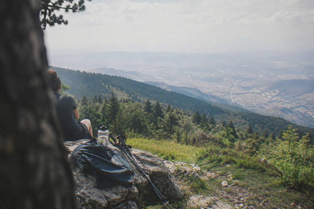 Walking poles, a water bottle and a folded rain jacket laid on a rock beside a trail