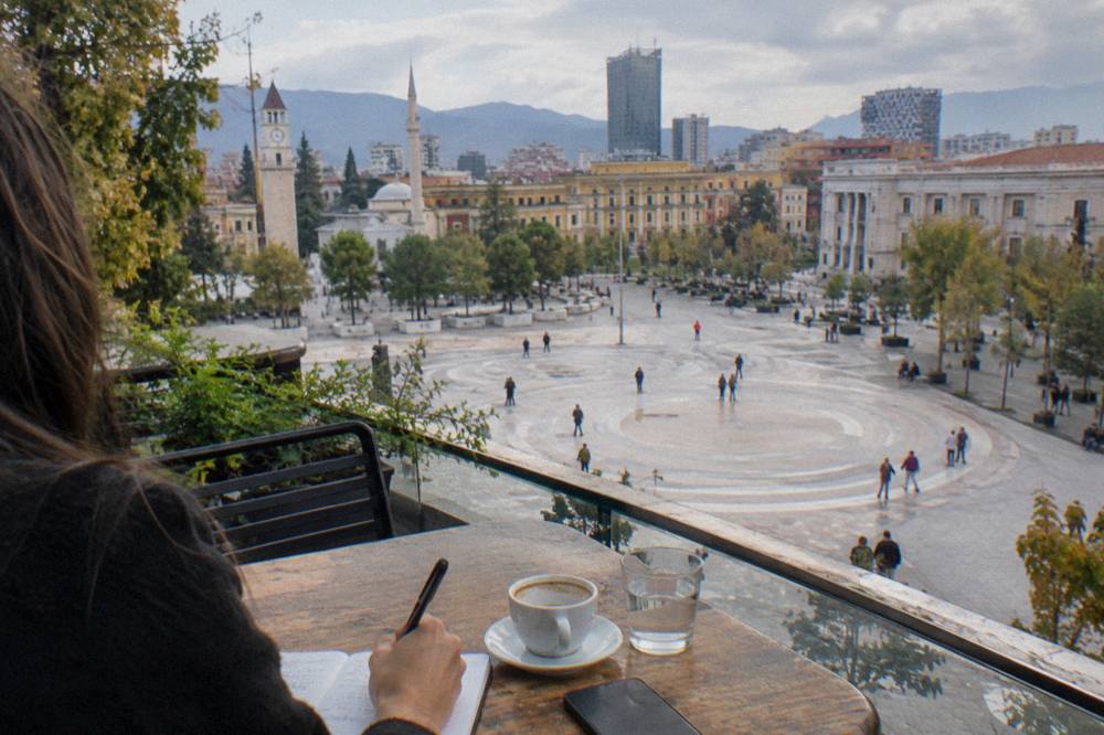 Person writing emergency contact numbers in a notebook on a cafe table in Tirana