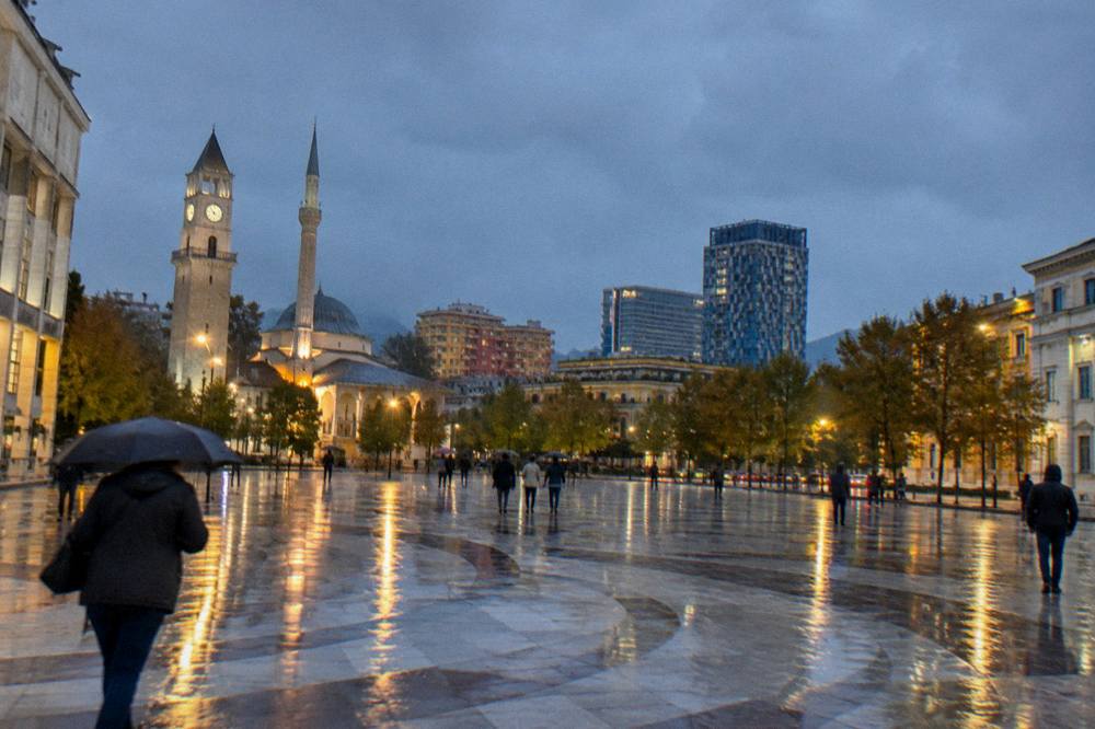 Rainy evening on a Tirana boulevard with reflections on the wet pavement and lit facades