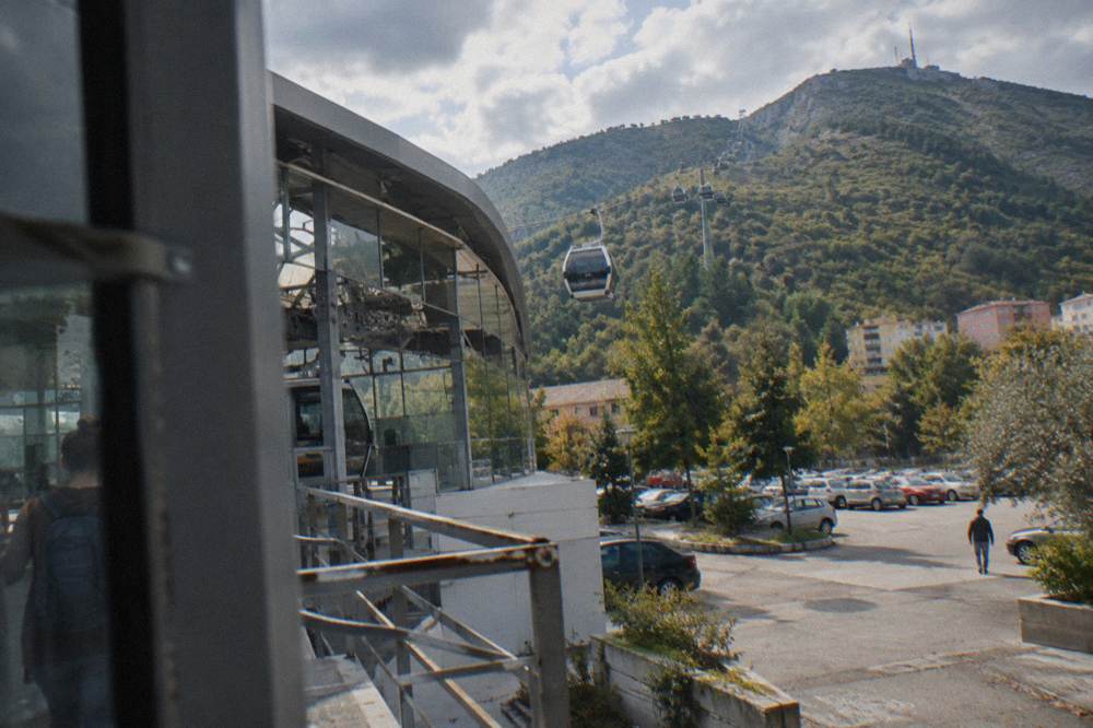 A cable car cabin rising above trees toward the ridge of Mount Dajti above Tirana