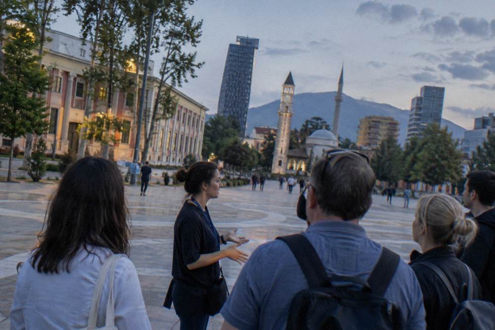 A tour guide speaking to a small group of visitors on a pedestrian street in central Tirana
