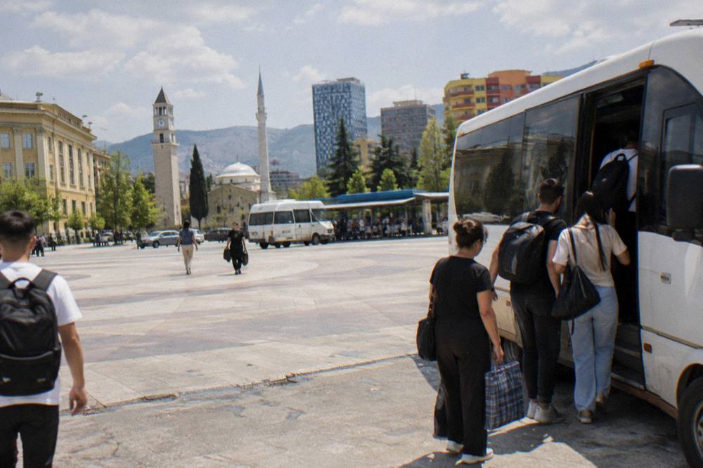 A minibus parked at an intercity bus terminal on the edge of Tirana with passengers boarding