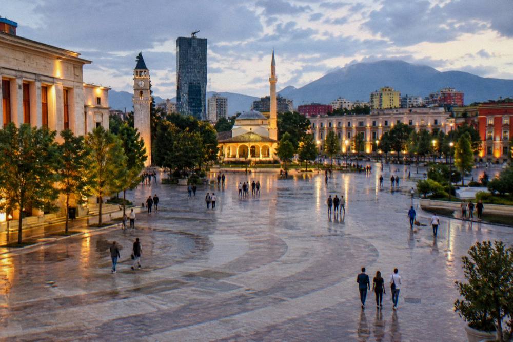 An evening view of Skanderbeg Square in Tirana with people strolling under lit facades
