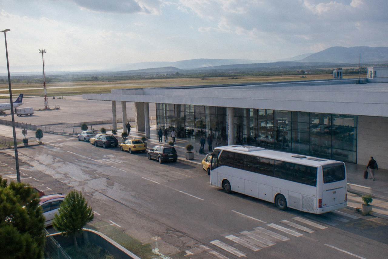 A bus waiting outside the terminal building at Tirana International Airport on a clear morning