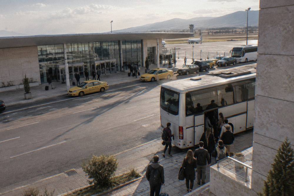 Passengers boarding a coach on a city street beside a grand stone building