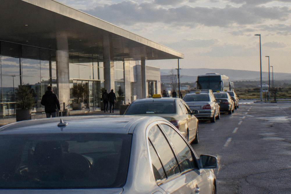 A line of taxis parked in a rank outside an airport terminal at dusk
