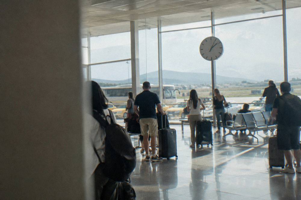 Travellers with suitcases waiting beside a clock in a bright airport arrivals hall