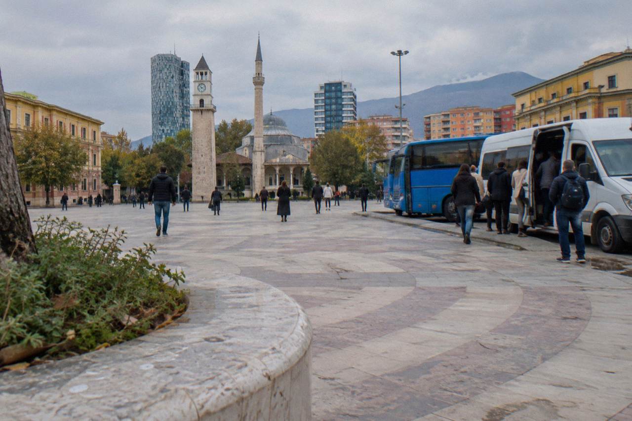 Buses parked at a bus terminal on the edge of Tirana with passengers boarding a minibus
