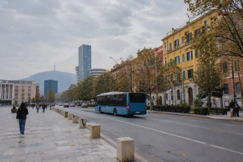 A city bus driving along a boulevard in Tirana past colourful buildings