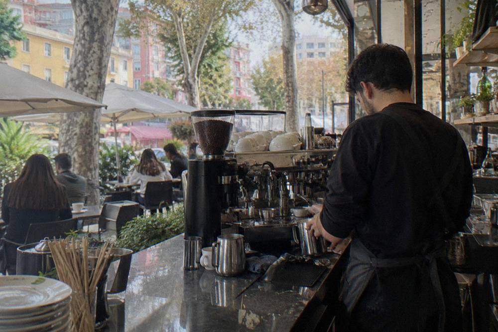 A barista preparing espresso drinks behind a busy Tirana cafe counter