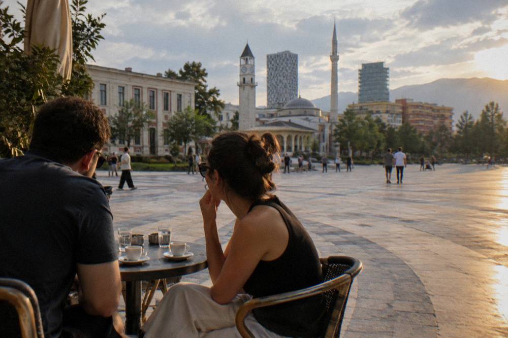 Two friends talking over espresso at a small round cafe table in Tirana