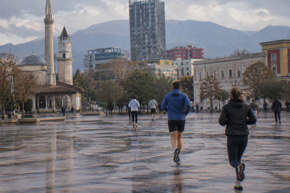 Runners passing Ottoman-era and modern buildings on a boulevard in central Tirana