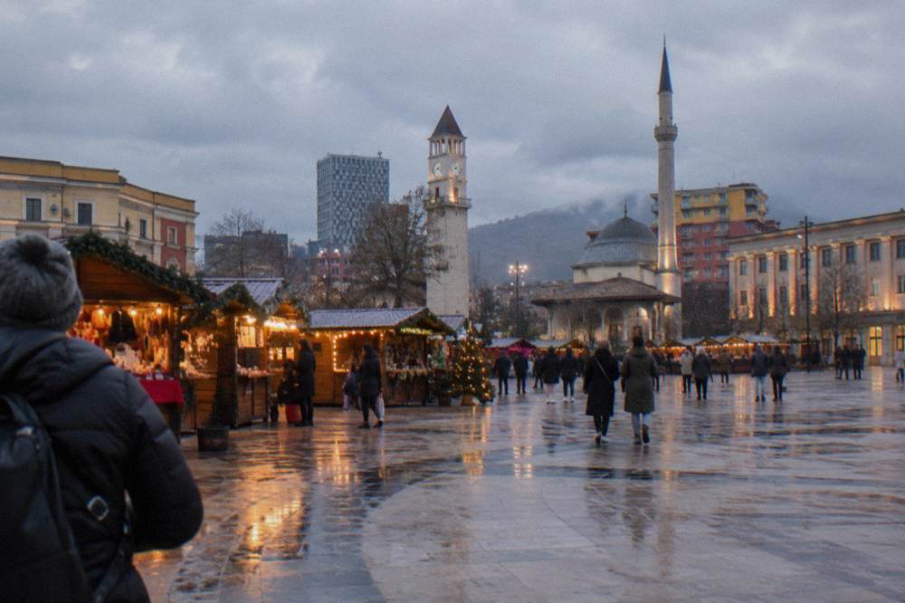 A Christmas market with wooden stalls and lights on a city square at dusk