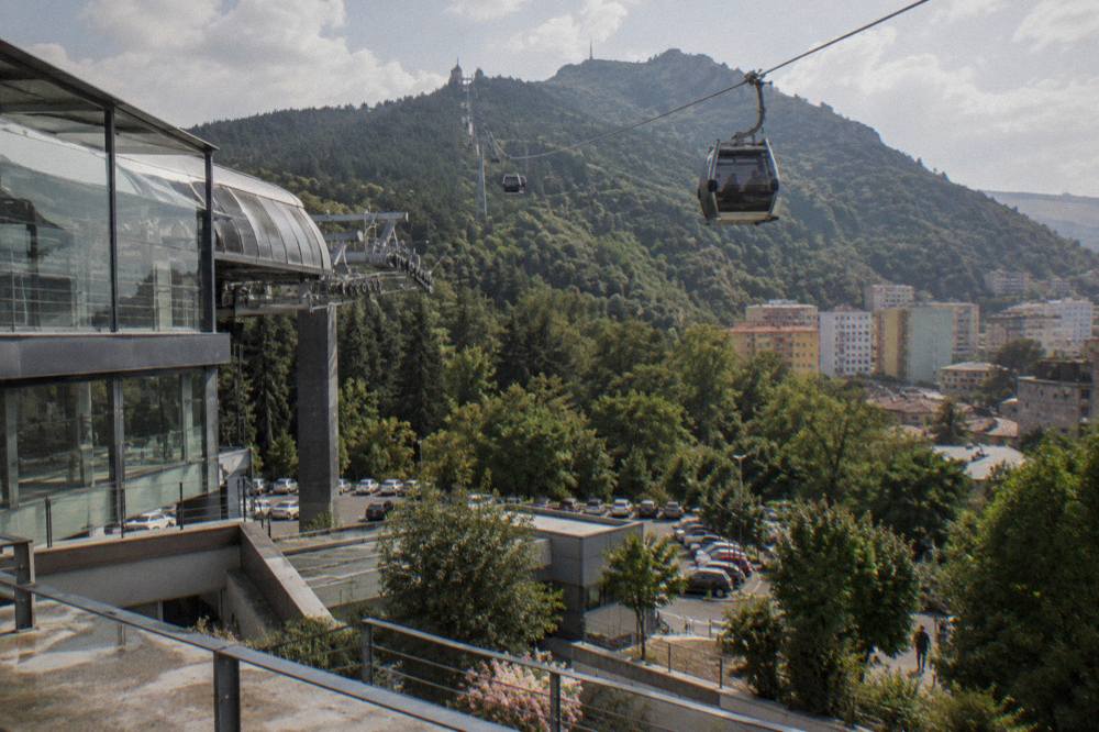 A cable car cabin rising above trees toward a mountain above the city
