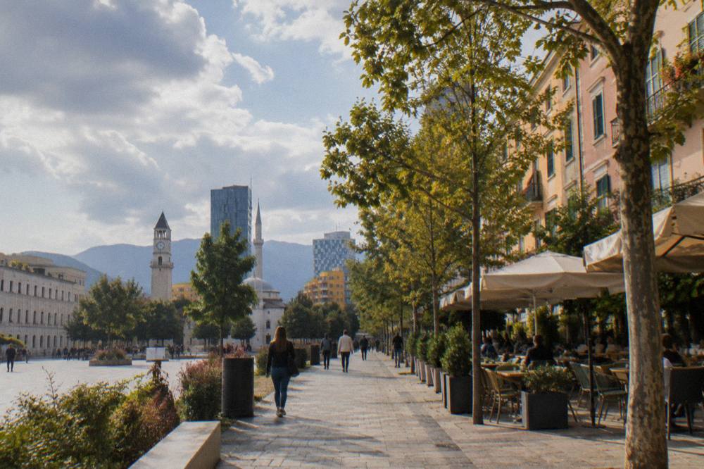 A tree-lined pedestrian boulevard in central Tirana with cafes and pastel buildings