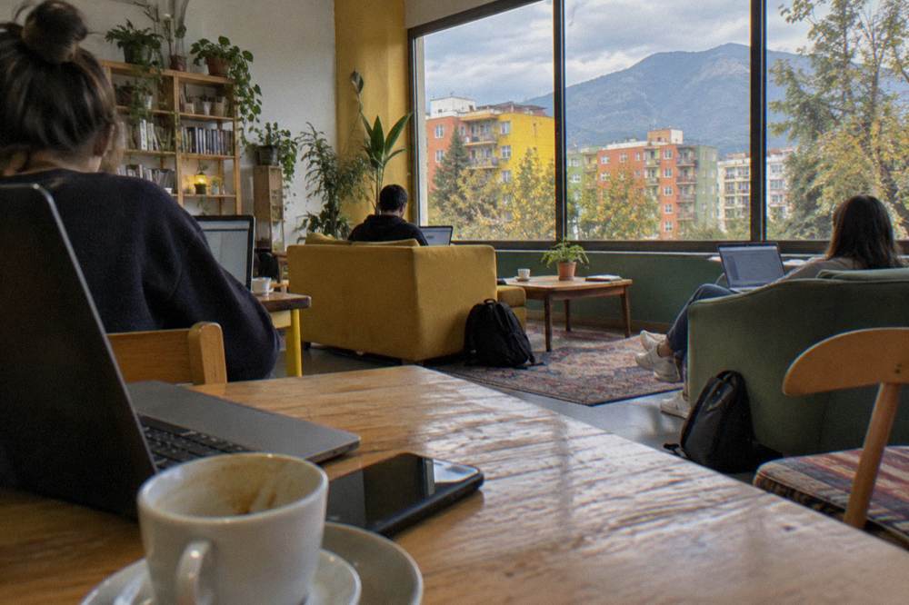 Travellers relaxing with laptops and coffee in a bright hostel common room