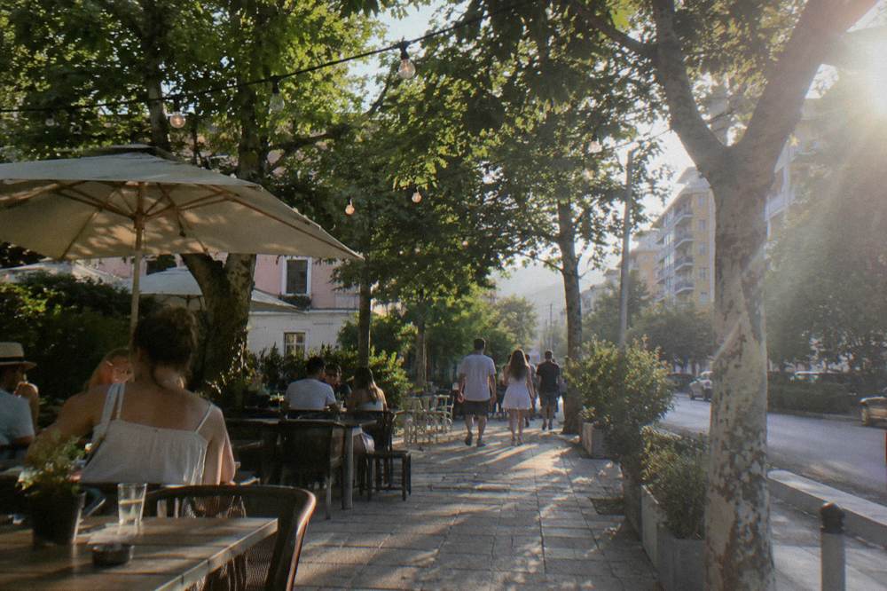 Cafe tables and string lights on a leafy Blloku street in Tirana at dusk