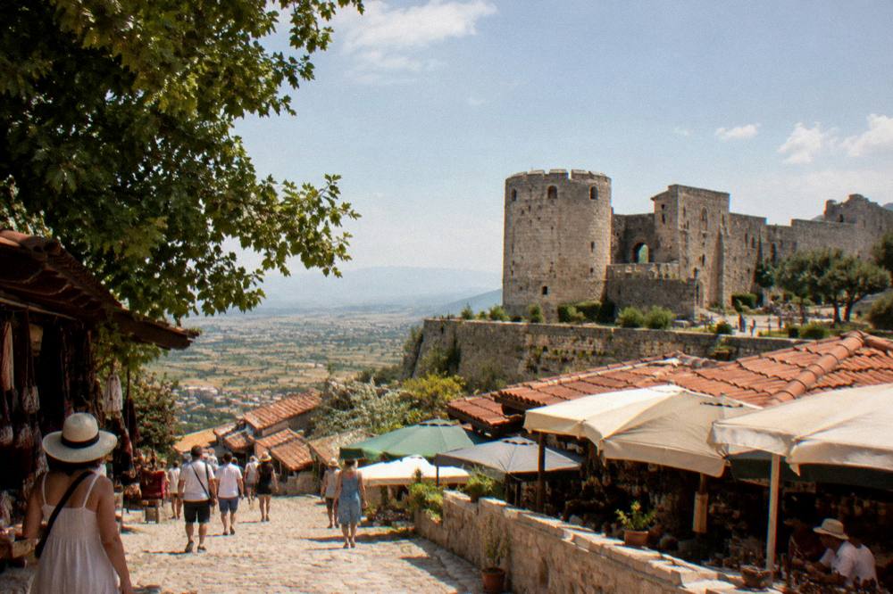 Stone walls of Kruja castle above a red-tiled bazaar street under a clear sky