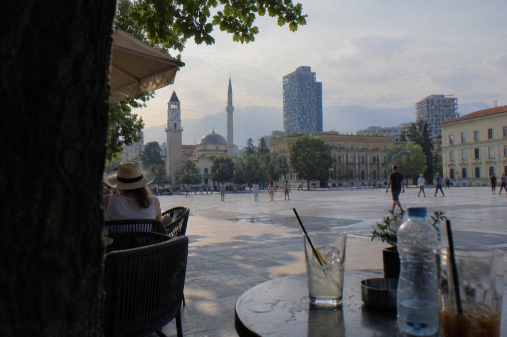 A shaded table with cold drinks and a water bottle on a Tirana cafe terrace in summer