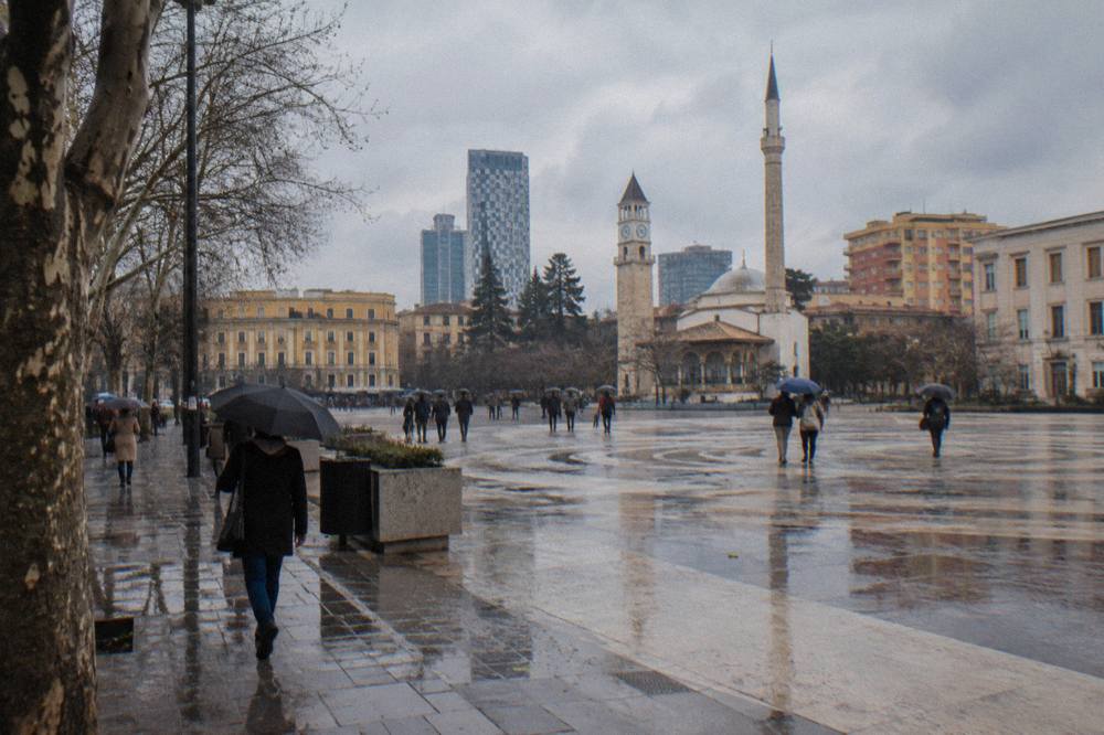 Rain-wet cobblestones and umbrella-carrying pedestrians on a Tirana street in winter