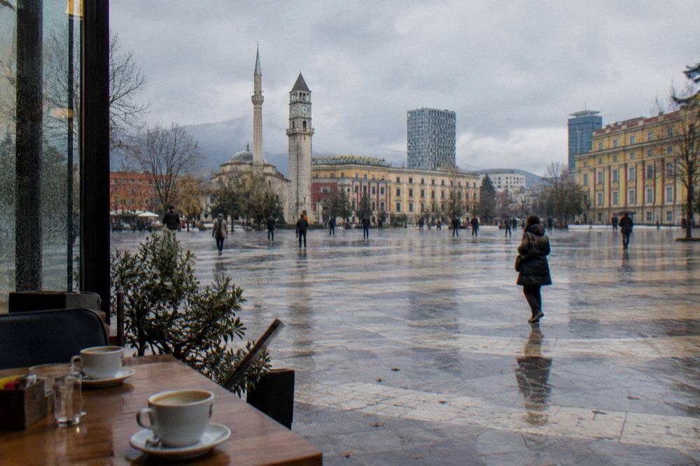 Warm cafe interior in Tirana with coffee cups on a wooden table and rain on the window