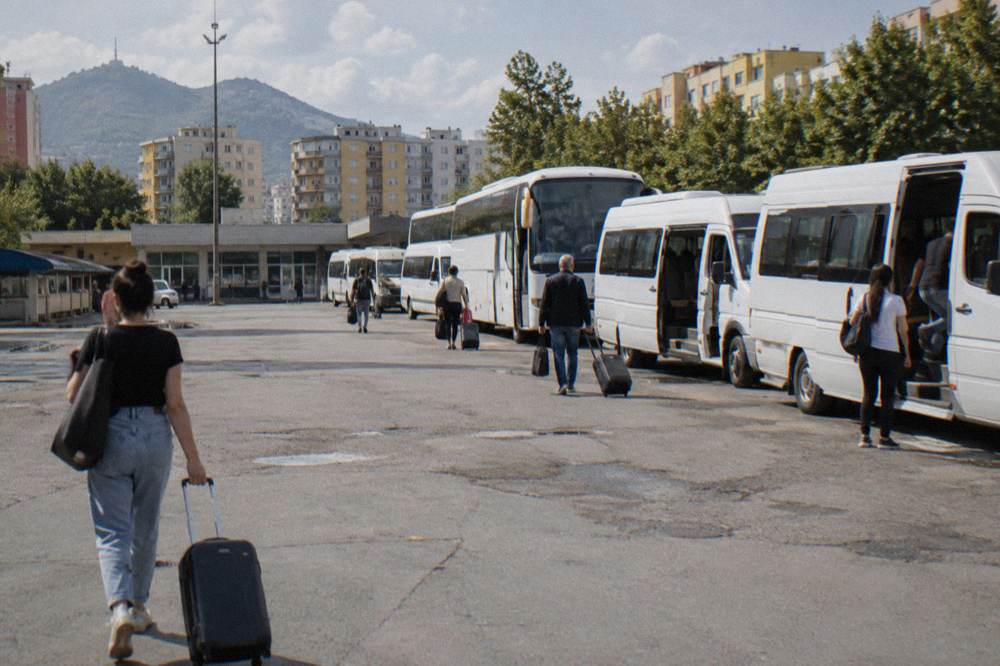 Intercity minibuses lined up at a bus terminal with passengers boarding in daylight