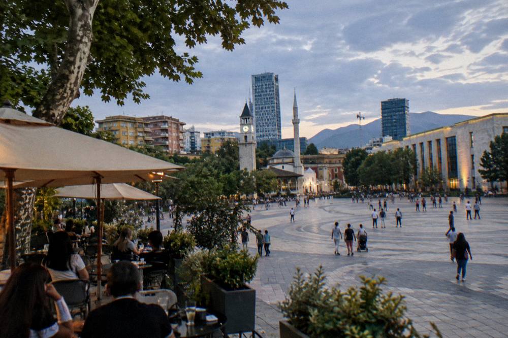Cafe tables and umbrellas on a leafy street in the evening with people seated talking