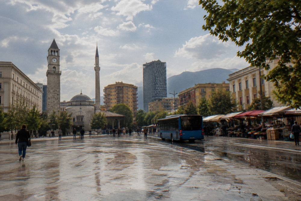 A city bus passing a street with market stalls and awnings in Tirana