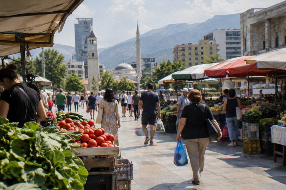 Shoppers browsing a busy open-air market street in Tirana in late afternoon light