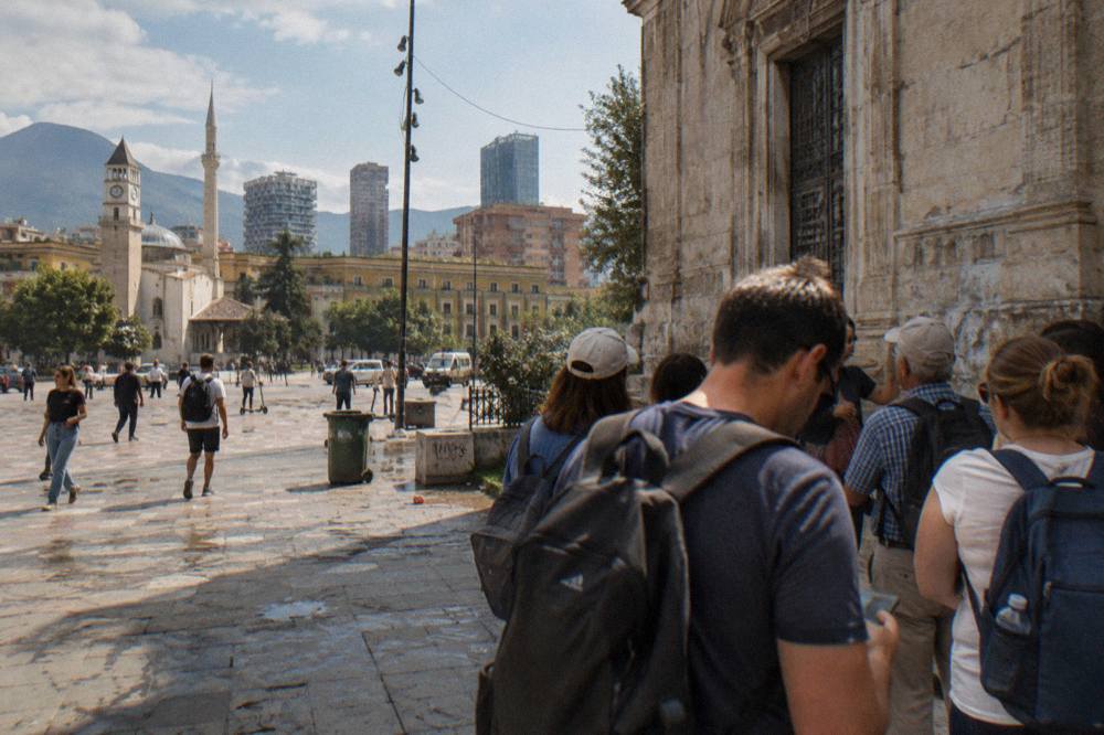 A guided walking group pausing at a historic building facade in central Tirana