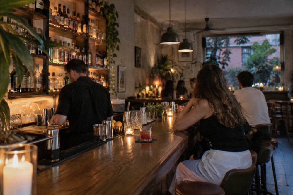 A candlelit cocktail bar interior with a long wooden counter in the Blloku district