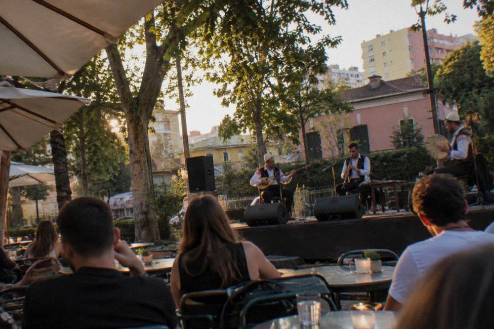 Musicians playing traditional Albanian instruments on a small stage during an evening performance