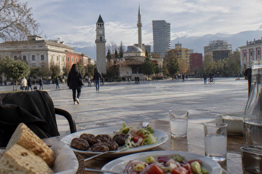 A table with grilled meatballs, salads, bread and small glasses of raki in a Tirana restaurant