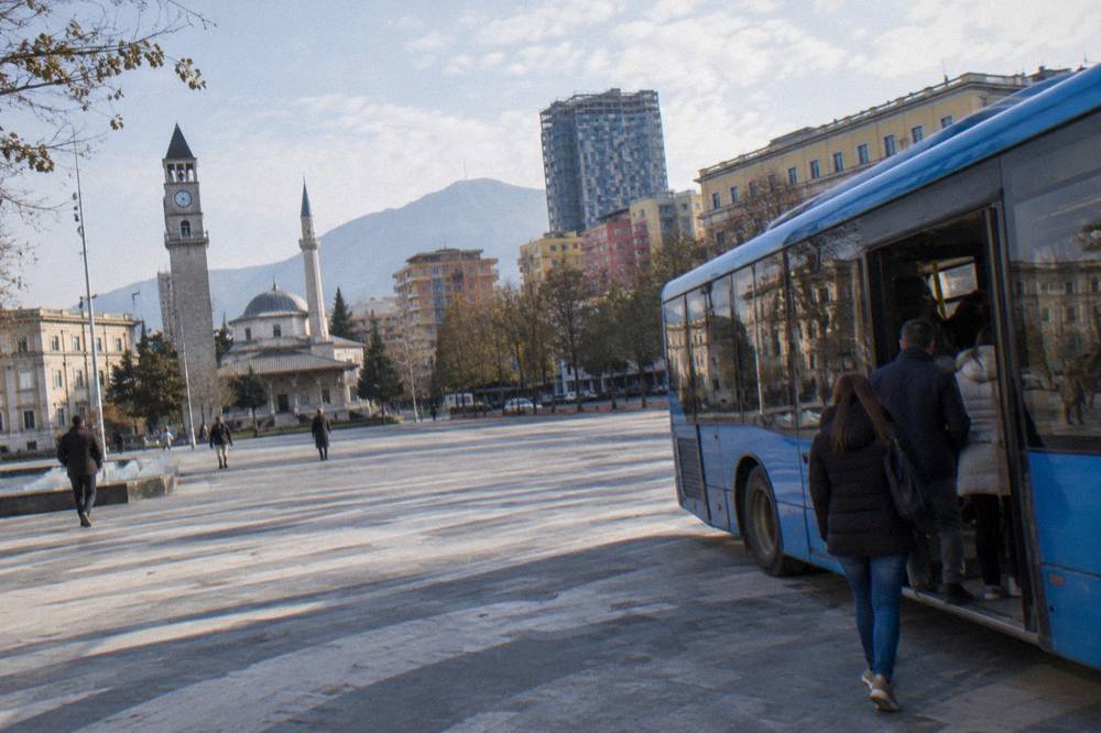 Blue city bus parked on a Tirana street with passengers boarding