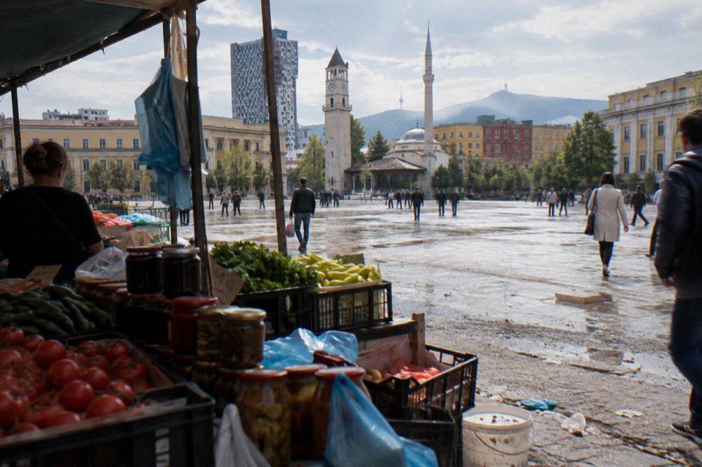 Fresh produce and jars of preserves stacked at a busy Tirana market stall