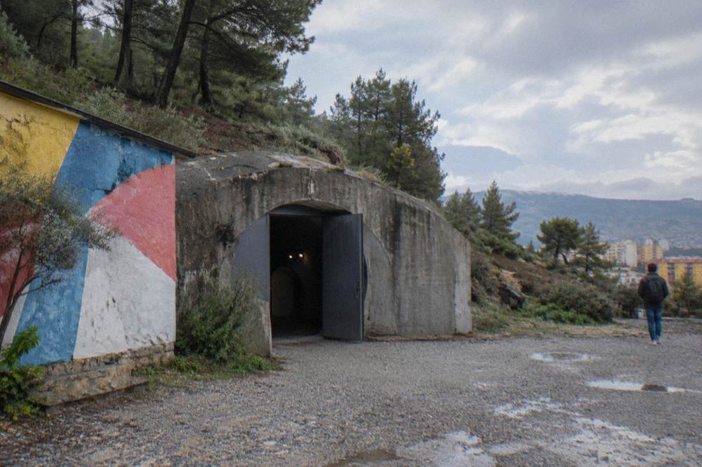 A grey communist-era bunker structure standing beside a colourful painted wall in Tirana