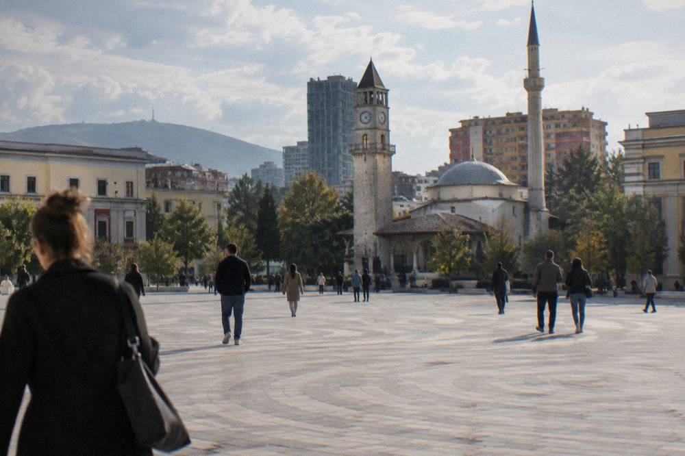 People walking across Skanderbeg Square in Tirana on a bright day with the mosque and clock tower behind