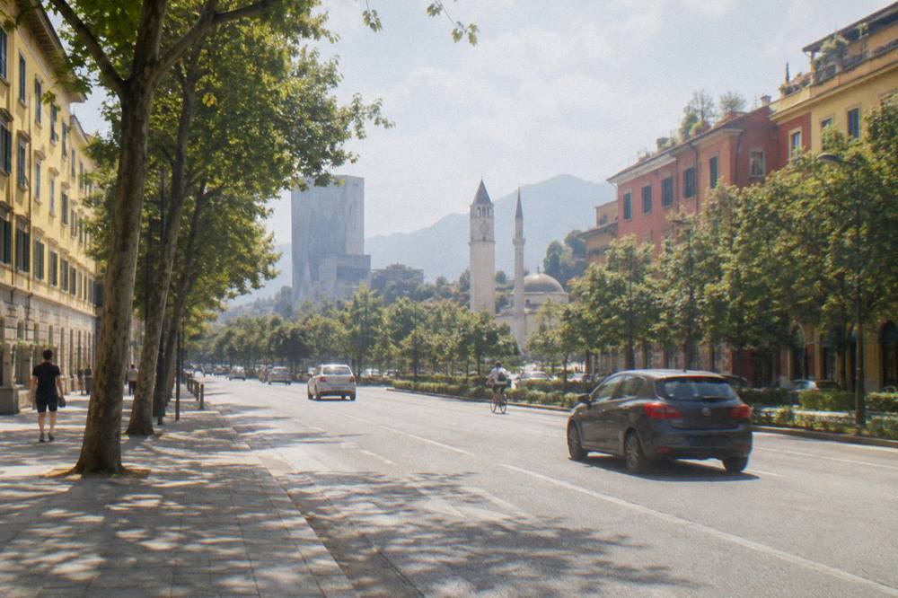A wide street in Tirana lined with colourful building facades and trees in daylight