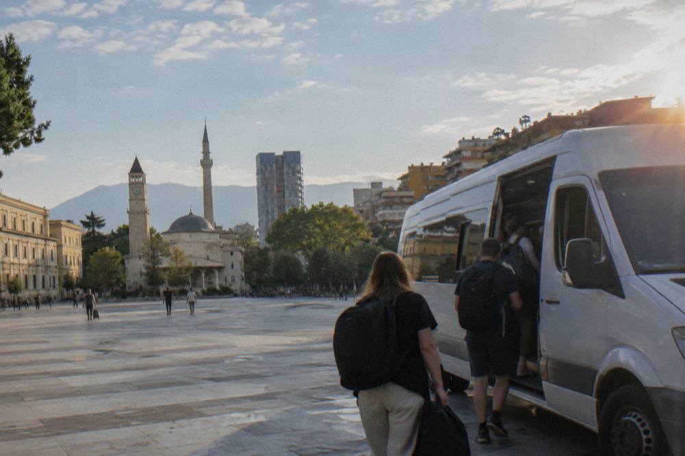 Passengers boarding a white intercity minibus at a terminal in Tirana