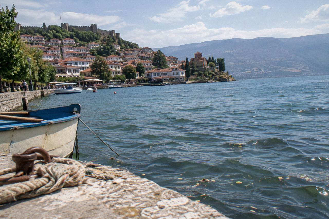 A long blue lake surrounded by wooded hills with an old town of red roofs on the shore