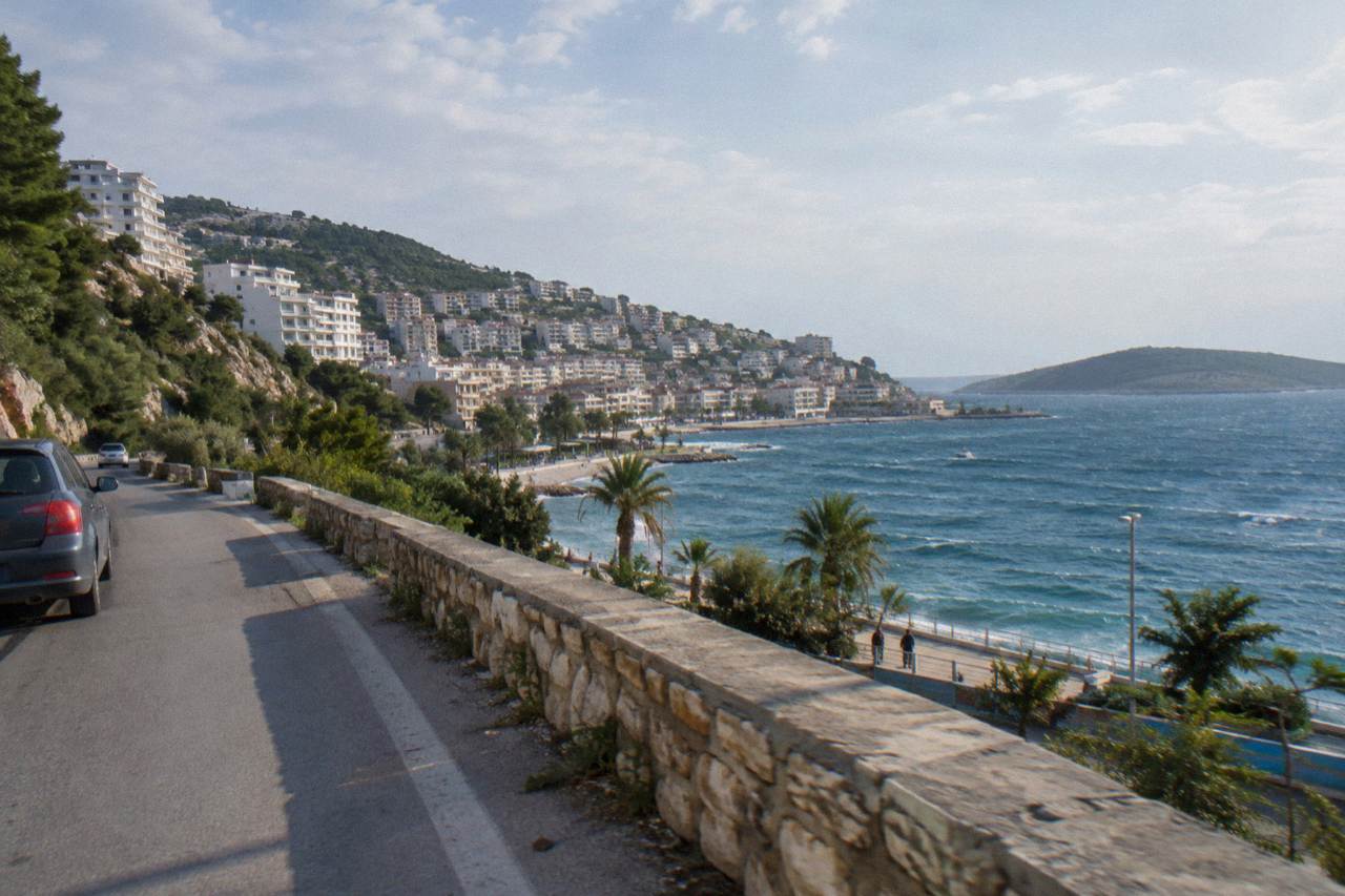 A coastal road curving along green hills above a blue bay in southern Albania