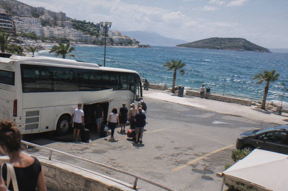A long-distance bus parked at a terminal with passengers loading luggage