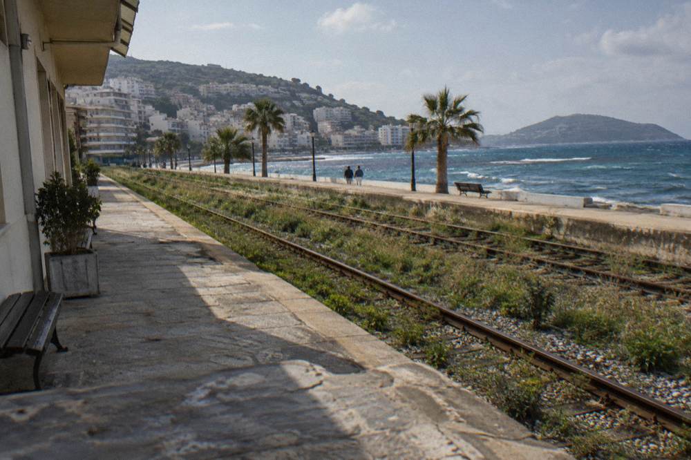 An empty rail platform with overgrown tracks beside a station building