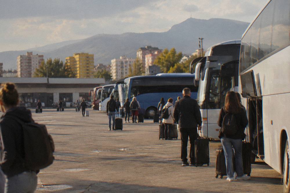 Passengers with suitcases waiting beside a row of coaches at an international bus terminal