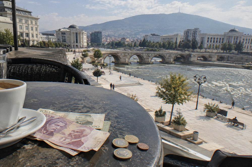 A handful of Albanian lek banknotes beside euro coins on a cafe table