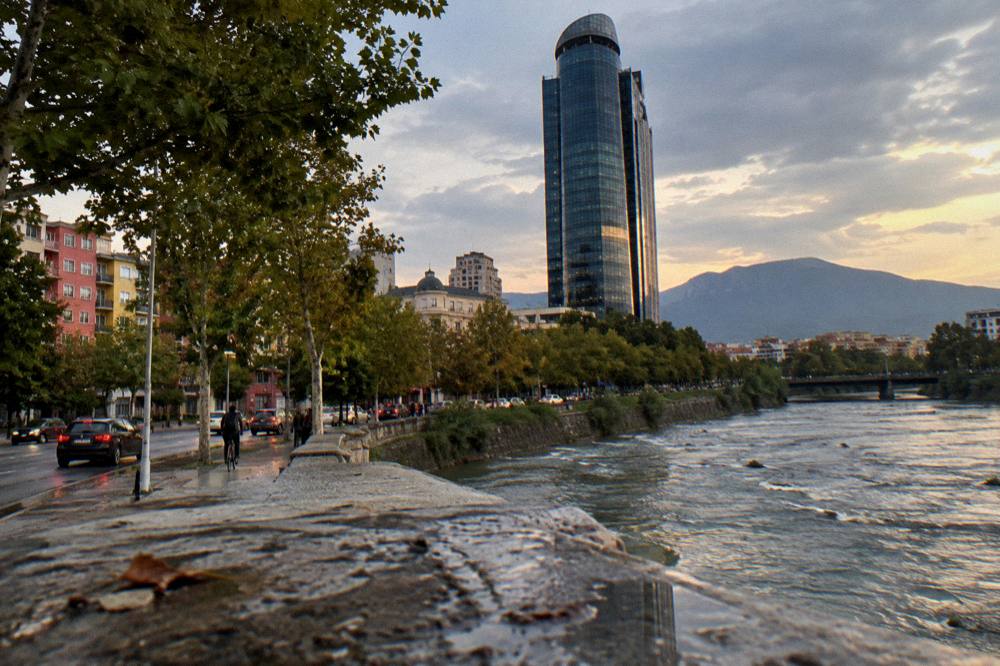 A tall tower building rising above tree-lined city streets at dusk