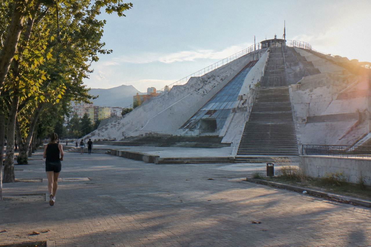 The concrete Pyramid of Tirana under a clear sky, with steps climbing its sloped facade